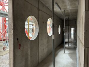 Betonflur in einem Rohbau mit runden Fensteröffnungen und Baugerüsten. Kühle, industrielle Stimmung durch graue Betontöne.