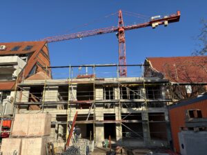 Im Bild ist ein mehrstöckiges Gebäude im Bau zu sehen, gerüstet mit einem Kran darüber, an einem klaren, sonnigen Tag.